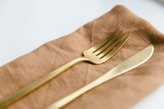 Golden colored cutlery styled on a orange linnen napkin.