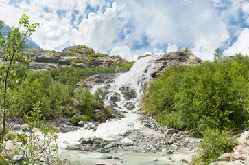 Beautiful waterfall. On a Sunny day the mountain stream flows among the forest .