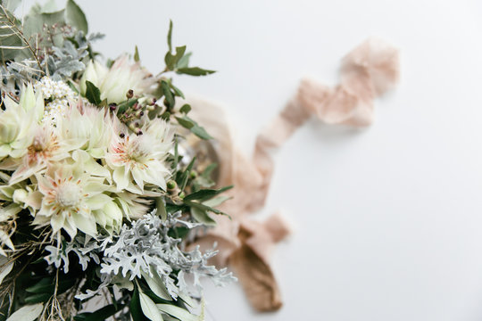 A wedding bouquet in soft green, beige and pink tones in a white neutral setting waiting for the bride on her special day.