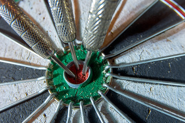 Darts in a dartboard. 3 darts in a bulls eye.