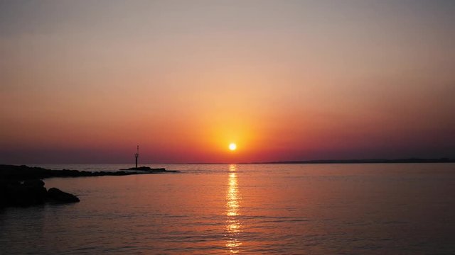 Timelapse of beautiful warm red sunset with sun rays reflected in calm ocean water
