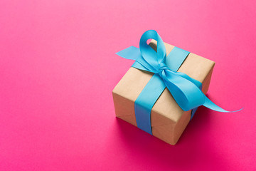 gift wrapped and decorated with blue bow on pink background with copy space. Flat lay, top view