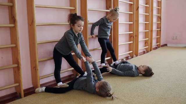Little girls warm up in the gym near the Swedish wall. Exercises in rhythmic gymnastics. Stretching muscles in the twine