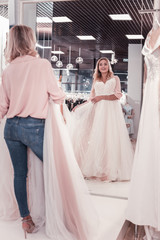 Naklejka premium Full length look. Positive beautiful woman standing in front of the mirror while looking at herself in wedding dress