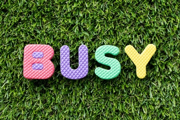 Color alphabet letter in word busy on artificial green grass background