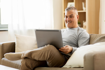 technology, people and lifestyle concept - man with laptop computer sitting on sofa at home