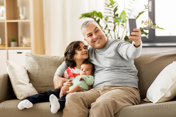 family, fatherhood and people concept - happy father with preteen and baby son taking selfie at home