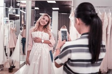 Modern technology. Pleasant brunette woman holding her smartphone while taking a photo of her friend