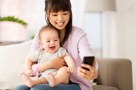 family and motherhood concept - happy smiling young asian mother with little baby son taking selfie by smartphone at home