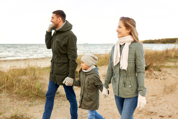 family, leisure and people concept - happy mother, father and little daughter walking along autumn beach