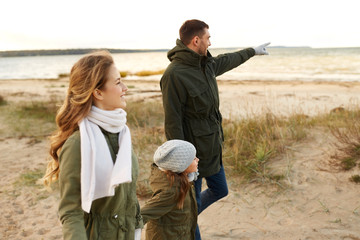 Fototapeta premium family, leisure and people concept - happy mother, father and little daughter walking along autumn beach