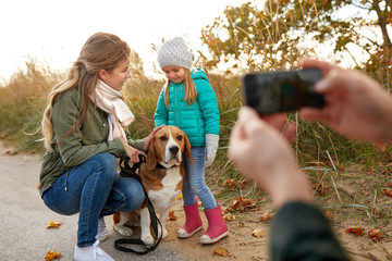 Fototapeta premium family, leisure and people concept - happy mother, father and little daughter photographing by smartphone on autumn beach
