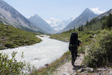 Man with a backpack walking along the path along the Akkem River, against the background of the Belukha Mountain, Altai, Russia