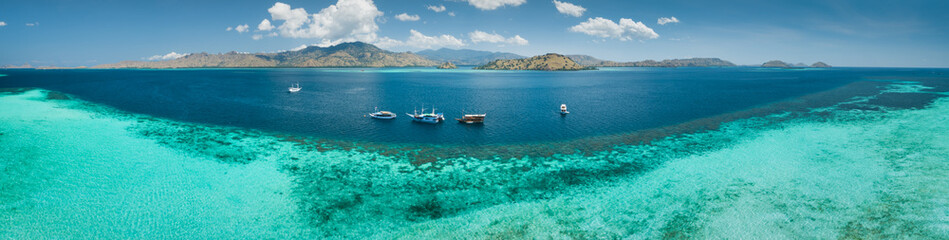 Naklejka na ściany i meble Aerial drone panoramic shot ocean, Komodo background. Transparent turquoise water of the Pacific ocean with the boats taken for tourist reasons. Komodo National Park, Indonesia.