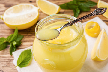 Homemade lemon curd in glass jars with fresh lemons, rustic wooden background copy space