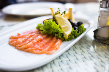 sliced smoked salmon served with lemon slices on white plate
