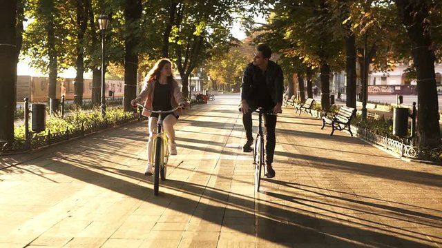 Front view of a young couple or friends riding their bikes in the city park or boulevard in summertime. People, leisure and lifestyle concept