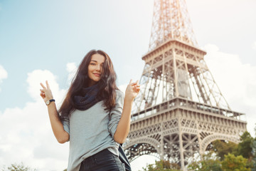 Young attractive happy woman showing peace gesture Eiffel Tower in Paris, France. Portrait of travel tourist girl on vacation walking happy outdoors. Gorgeous mixed race Asian Caucasian female