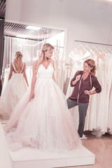 Naklejka premium Professional service. Nice female tailor holding her glasses while looking at the bride