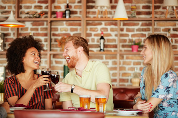 Group of friends having dinner at restaurant. Friends cheering and drinking alcohol.