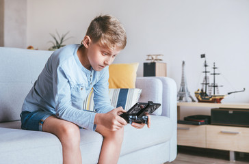 Teenager boy enthusiastically plays on the game console connected with smartphone