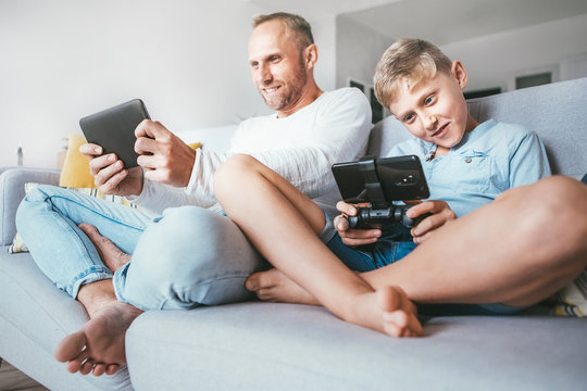Father and son enthusiastically playing  the electronic devices : tablet and gamepad sitting in living room