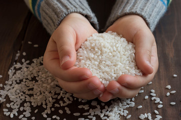 baby hands holding rice on wooden background