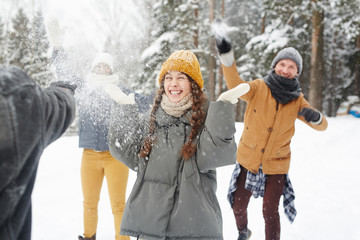 Happy young friends in winter coats having snowball fight in forest: excited girl standing in...