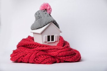 house in winter - heating system concept and cold snowy weather with model of a house wearing a knitted cap