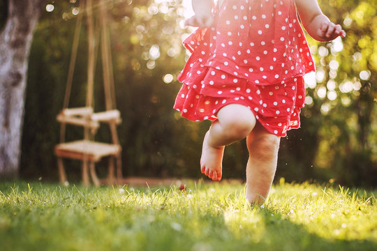 Little Girl's Bare Feet In The Grass. Little Girl Running  At Sunset