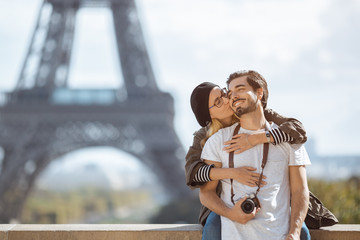 Paris Eiffel tower romantic tourist couple embracing kissing in front of Eiffel Tower, Paris, France. Dating couple posing in casual trendy clothes near outdoor. Handsome man with camera and cute
