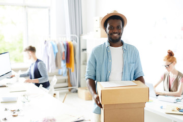 Portrait of smiling African man holding parcels with other people working in the background at workshop