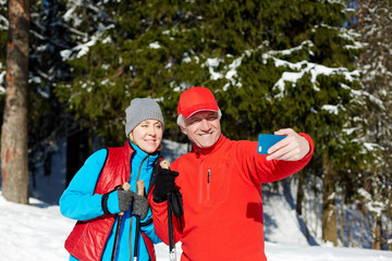 Happy seniors in winter activewear making selfie on smartphone during skiing training in the forest