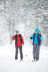 Sporty mature spouses in activewear skiing in snowfall at leisure on winter day