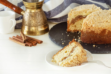 Cinnamon crumble coffee cake and jezva. White wooden background. Autumn cozy baking.