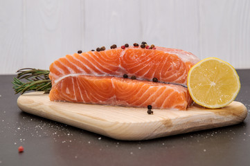 Close up. Ingredients. Fresh salmon filet surrounded by lemon, spices and herbs on a wooden board. Black and white background.