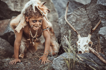 Caveman, manly boy hunting outdoors. Prehistoric tribal boy outdoors on nature. Young shaggy and dirty savage, warrior and hunter hiding in an ambush behind a stone in cave. Primitive ice age man in