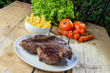 Round dish with grilled porterhouse beef steak on wooden table