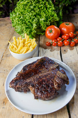 Round dish with grilled porterhouse beef steak on wooden table