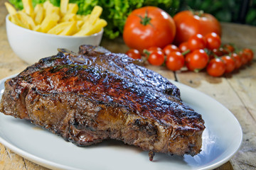 Round dish with grilled porterhouse beef steak on wooden table