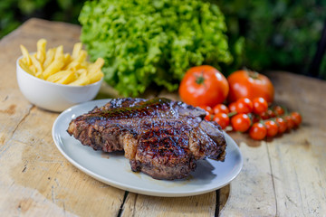 Round dish with grilled porterhouse beef steak on wooden table
