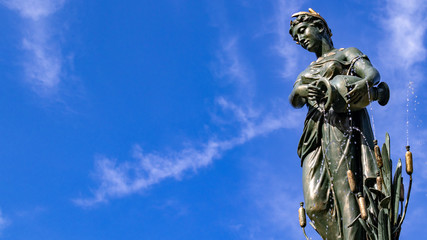 Fototapeta premium Female bronze statue with cloudy blue sky background, public gardens, autumn sunshine.