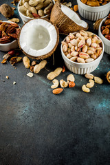 Various types of nuts - walnuts, pecans, peanuts, hazelnuts, coconut, almonds, cashews, in bowls, on a dark blue concrete table top view