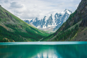 Fototapeta na wymiar Shine water in mountain lake in highlands. Wonderful giant snowy mountains. Creek flows from glacier. White clear snow on ridge. Amazing atmospheric landscape of majestic Altai nature.