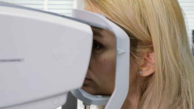 Woman looking at refractometer eye test machine in ophthalmology.
