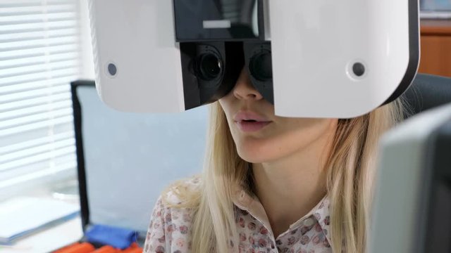 Young woman looking at refractometer eye test machine in ophthalmology.