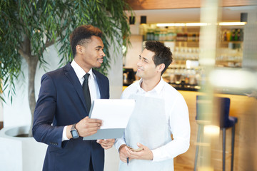 African businessman standing and discussing the menu with the waiter at restaurant