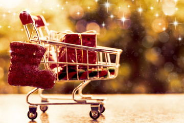 Xmas decorative items in mini shopping cart or trolley against blurred natural green background for Christmas and New Year festival concept (added glowing star and color filter effect)