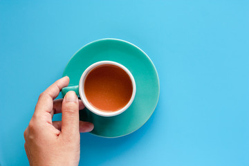 Hand holding cup of coffee with saucer on blue background for drinks and beverage concept