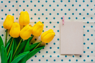 Artificial yellow tulips with white paper card on blue polka dot fabric or tablecloth for nature and springtime concept